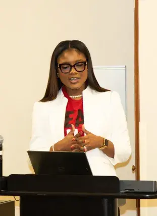 Shaneil McKenzie-Guyher at a podium, reading off a laptop