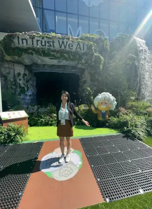 Linda Trinh standing outside, in front of a sign that says, "In Trust We AI"