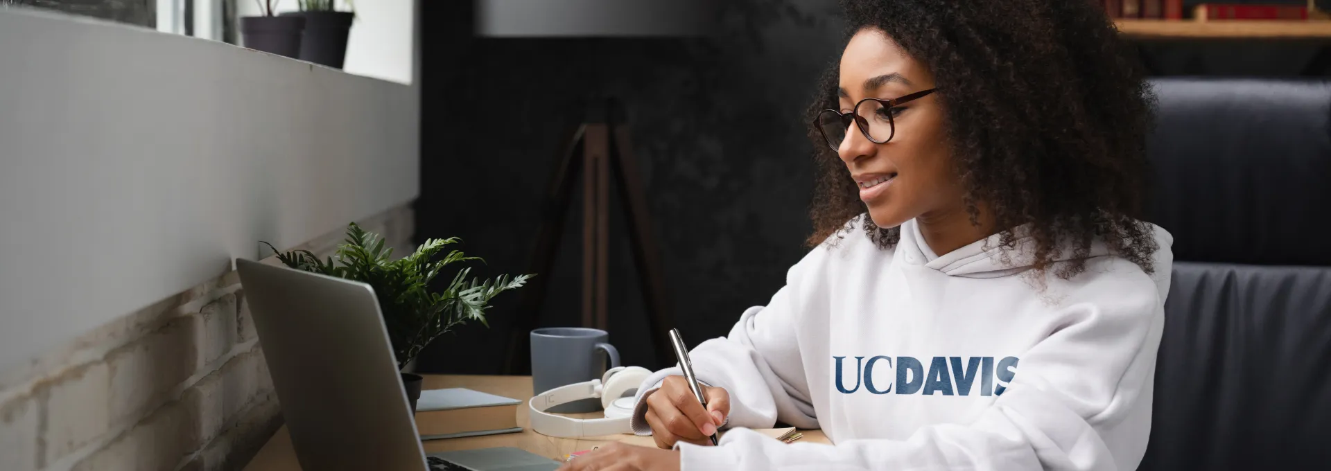 Woman sitting at laptop wearing a UC Davis sweatshirt