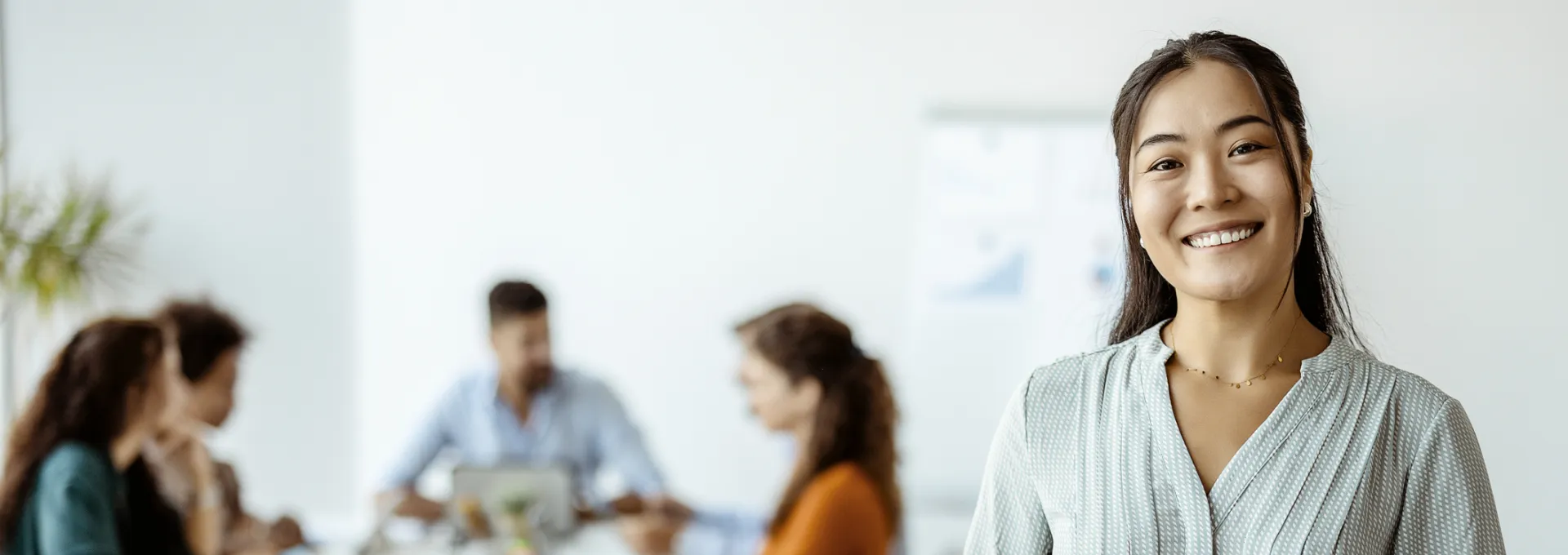Confident young Asian businesswoman standing smiling at the camera in a boardroom with colleagues in the background