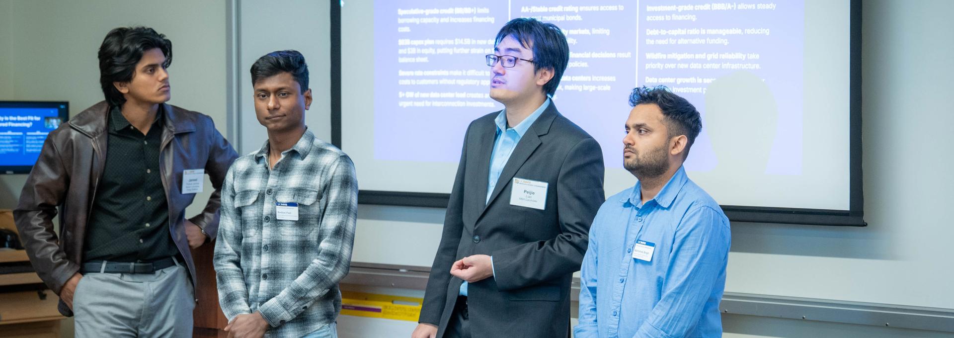 Four GSM students giving a presentation in front of a projector and screen