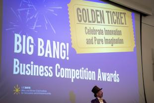 A person in a Willy Wonka costume stands in front of a projection reading "BIG BANG! Business Competition Awards" and "GOLDEN TICKET Celebrate Innovation and Pure Imagination.