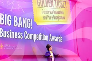 A person dressed as Willy Wonka stands in front of a screen displaying “BIG BANG! Business Competition Awards” and “Golden Ticket: Celebrate Innovation and Pure Imagination.”