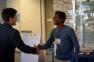 Two men shaking hands and smiling at a networking event.