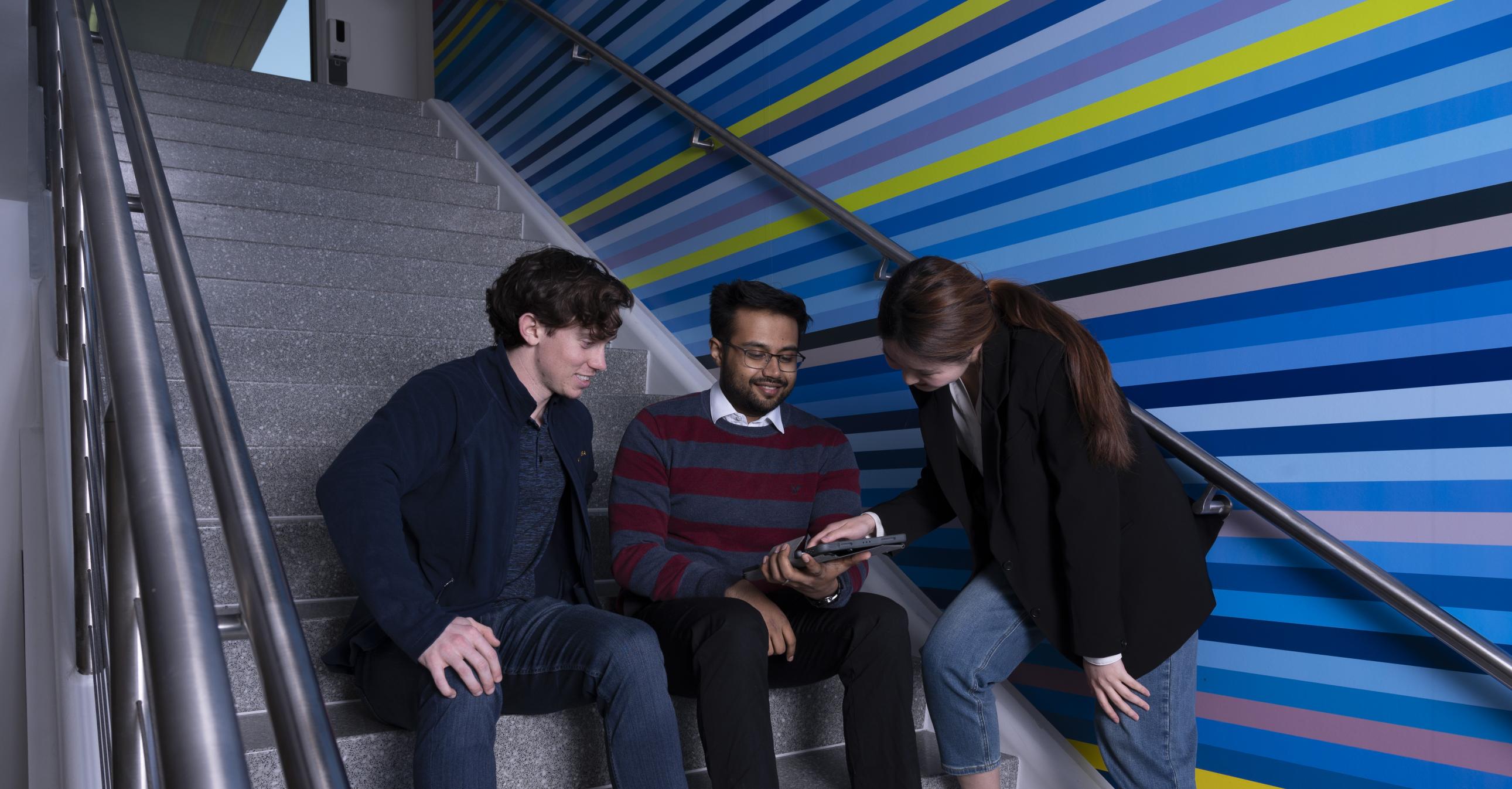 Group of individuals sitting on stairs looking at a tablet