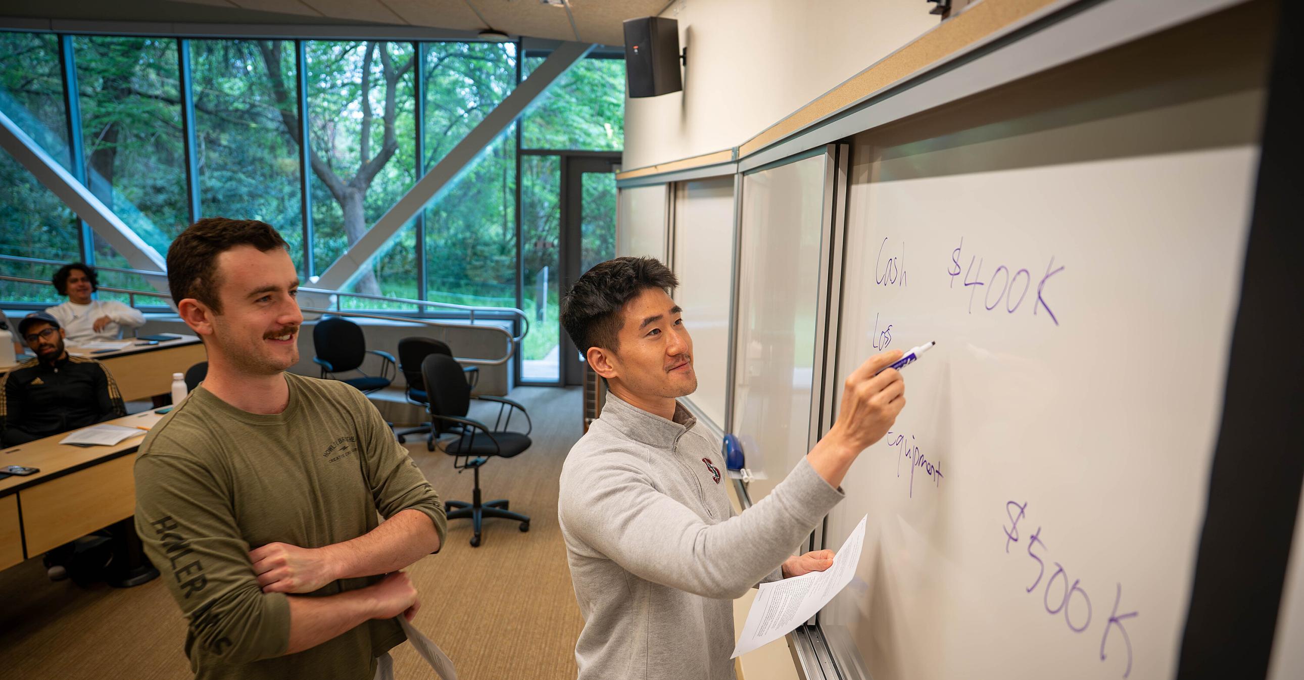 Two students at the front of a GSM classroom writing on a whiteboard