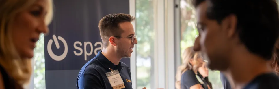 A group of people networking at a professional event, some wearing name tags and holding papers.