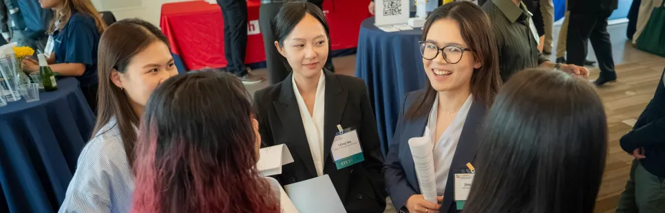 A group of people networking at a professional event, some wearing name tags and holding papers.