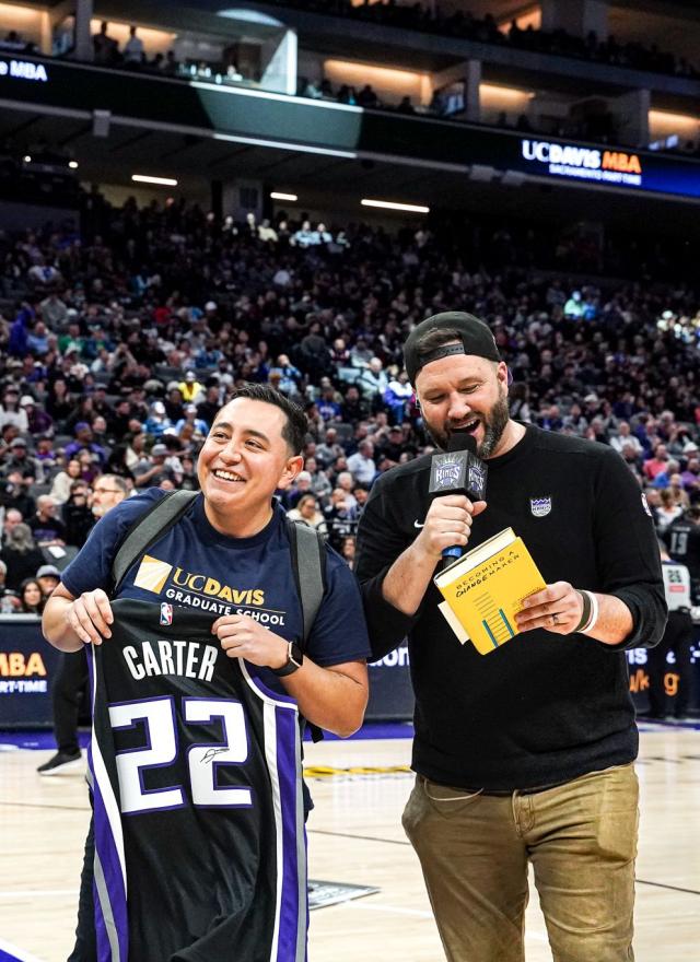Eddie Ramirez standing on the Sacramento Kings court, holding up a basketball jersey