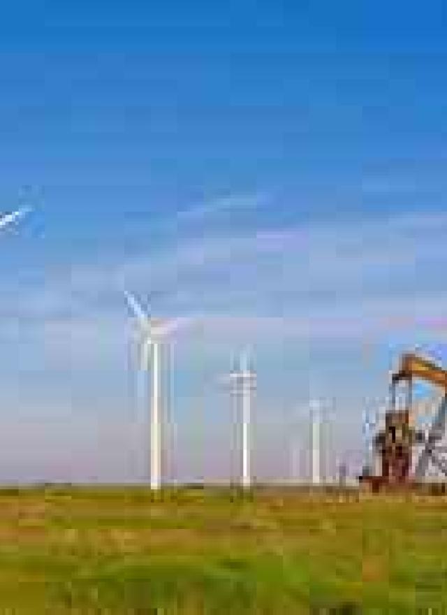 Wind turbines and an oil pumpjack stand side by side in a grassy field under a clear blue sky, symbolizing the contrast between renewable energy and fossil fuels.