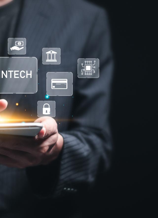 Person in a business suit using a smartphone, with floating digital icons representing financial technology (fintech) services such as data charts, banking, digital payments, and cybersecurity.