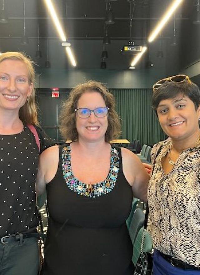 Jaimie Asakawa and two women stand together smiling inside a conference-style room with colorful chairs and tables in the background.