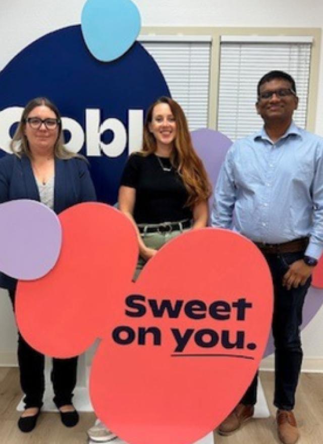Three people stand in front of an Oobli display sign inside an office, holding colorful cutouts with the phrase “Sweet on you.”