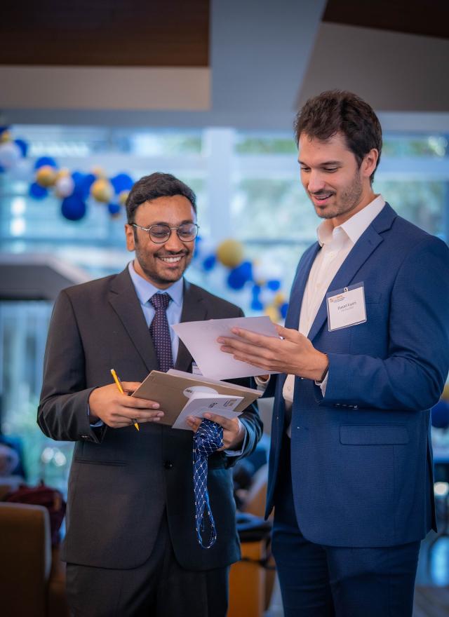 Daniel Vaziri and an MBA student reviewing documents during orientation, with blue and gold balloons decorating the background.