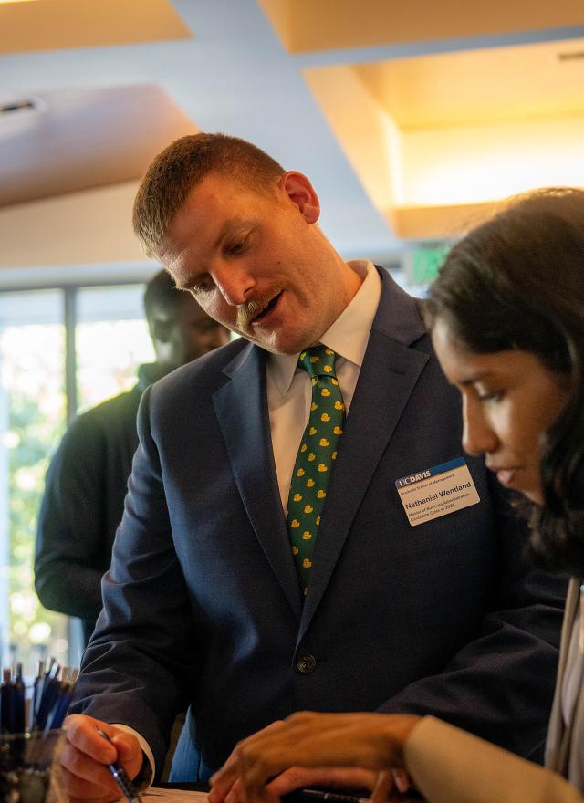 Nathaniel Wentland in a suit at Gallagher Hall, talking to other MBA students