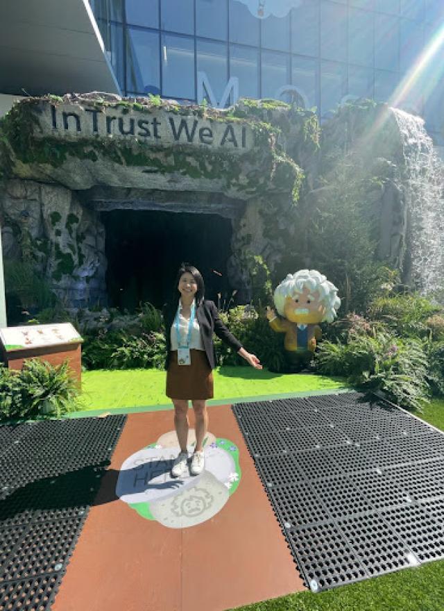 Linda Trinh standing outside, in front of a sign that says, "In Trust We AI"