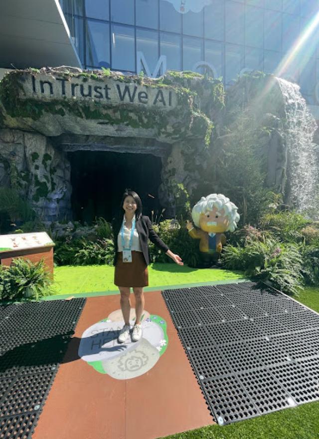 Linda Trinh standing outside, in front of a sign that says, "In Trust We AI"