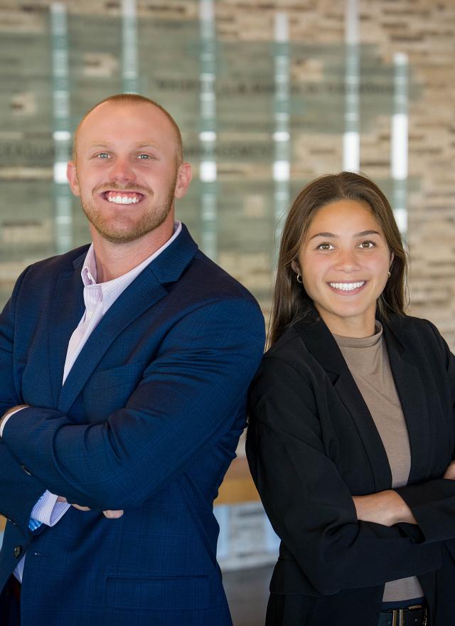 Two students standing back to back with their arms crossed, smiling at the camera