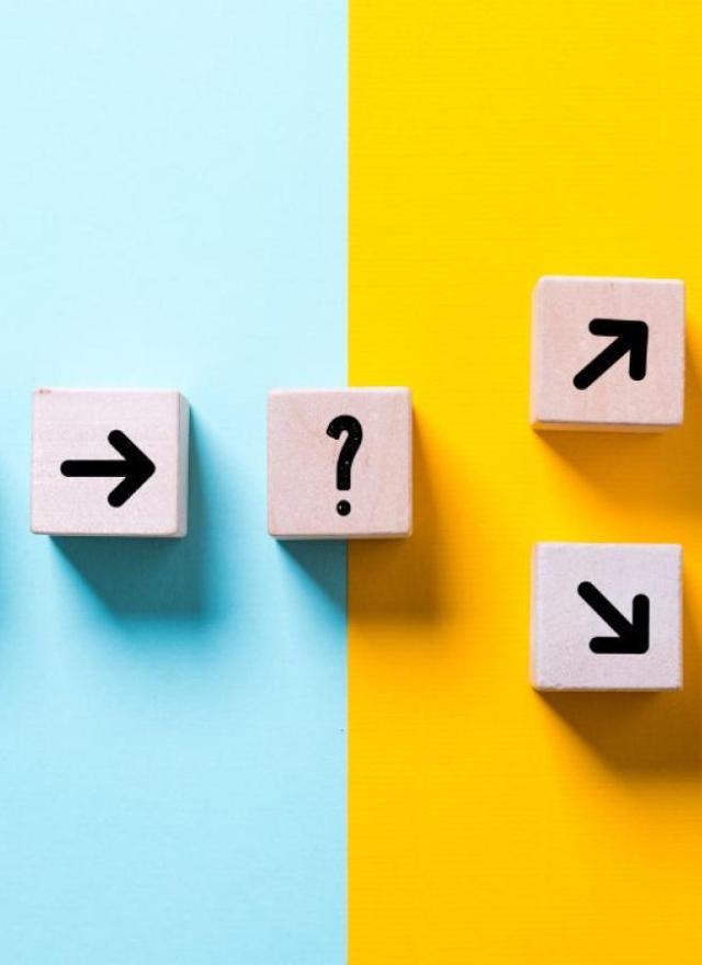 Wooden blocks with black arrows and a question mark form a path, transitioning from a light blue background to a yellow background with arrows going upward.