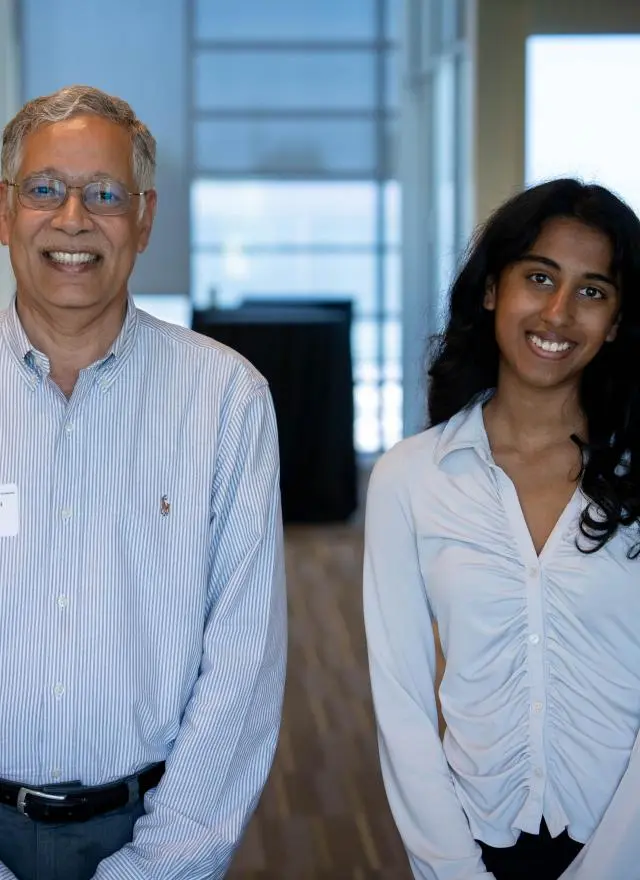 Dean Unnava and Rachel Johnson side by side in a hallway, both wearing light-colored shirts and smiling at the camera.