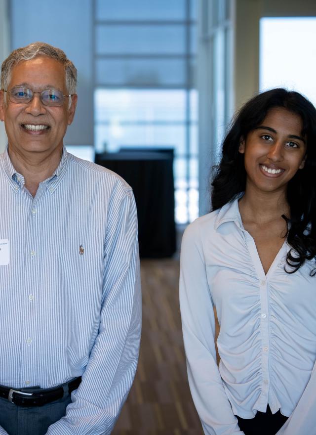 Dean Unnava and Rachel Johnson side by side in a hallway, both wearing light-colored shirts and smiling at the camera.