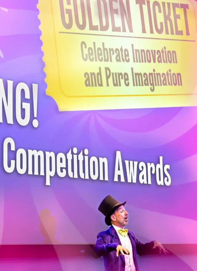 A person dressed as Willy Wonka stands in front of a screen displaying “BIG BANG! Business Competition Awards” and “Golden Ticket: Celebrate Innovation and Pure Imagination.”