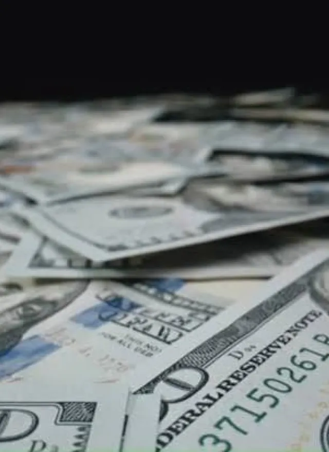 A pile of scattered United States one hundred dollar bills, showing Benjamin Franklin’s portrait and various security features.