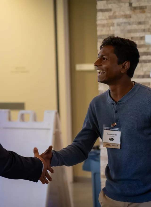 Two men shaking hands and smiling at a networking event.