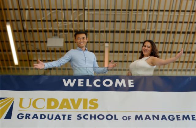 Two individuals posing in front of UC Davis Graduate School of Management banner