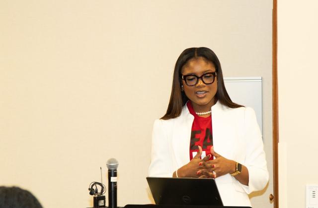 Shaneil McKenzie-Guyher at a podium, reading off a laptop