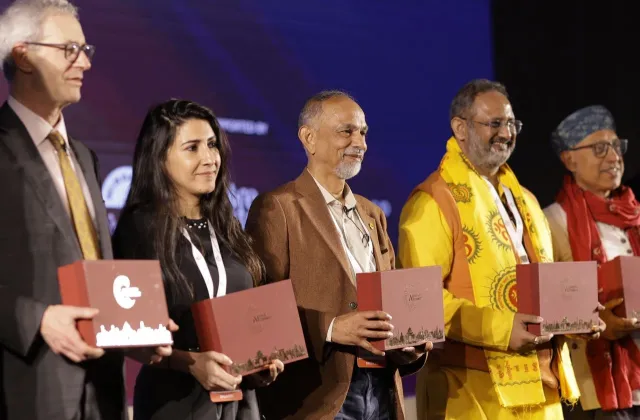 Five people stand on a stage holding matching red commemorative boxes during an awards presentation.