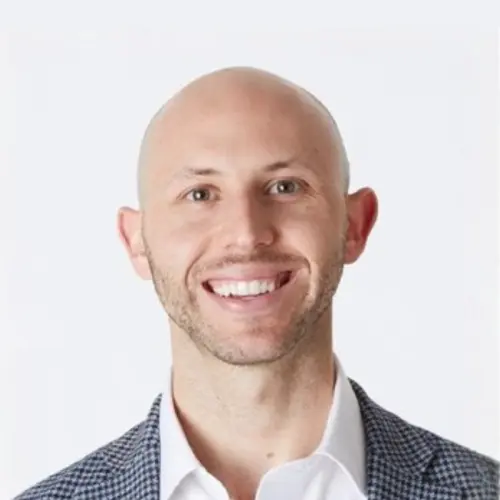 A smiling bald man wearing a white shirt and a checkered blazer, posed against a plain white background.