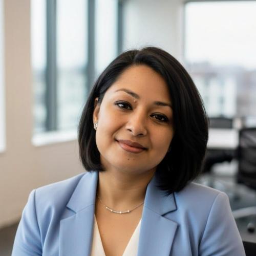 A woman with short dark hair wearing a light blue blazer and white top sits in a modern office with large windows.