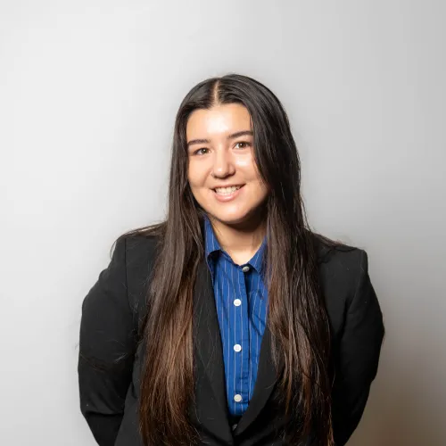 A young woman with long dark hair wearing a black blazer over a blue pinstriped button-down shirt.