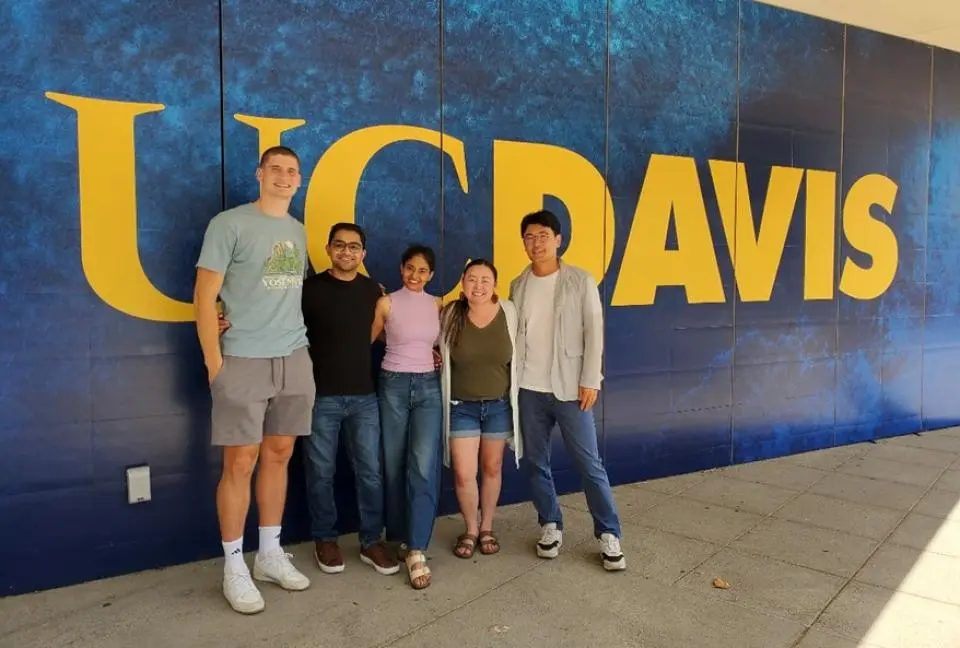 Maikhou Thao with four other MBA students, standing in front of a blue and gold UC Davis backdrop