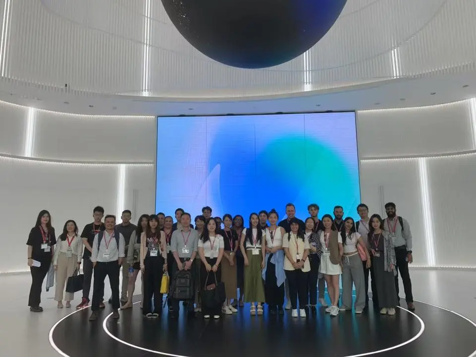 Group of UC Davis Graduate School of Management students and international peers standing together inside ByteDance headquarters in China. They are posed in front of a large digital display and surrounded by a modern, high-tech interior with glowing white walls.