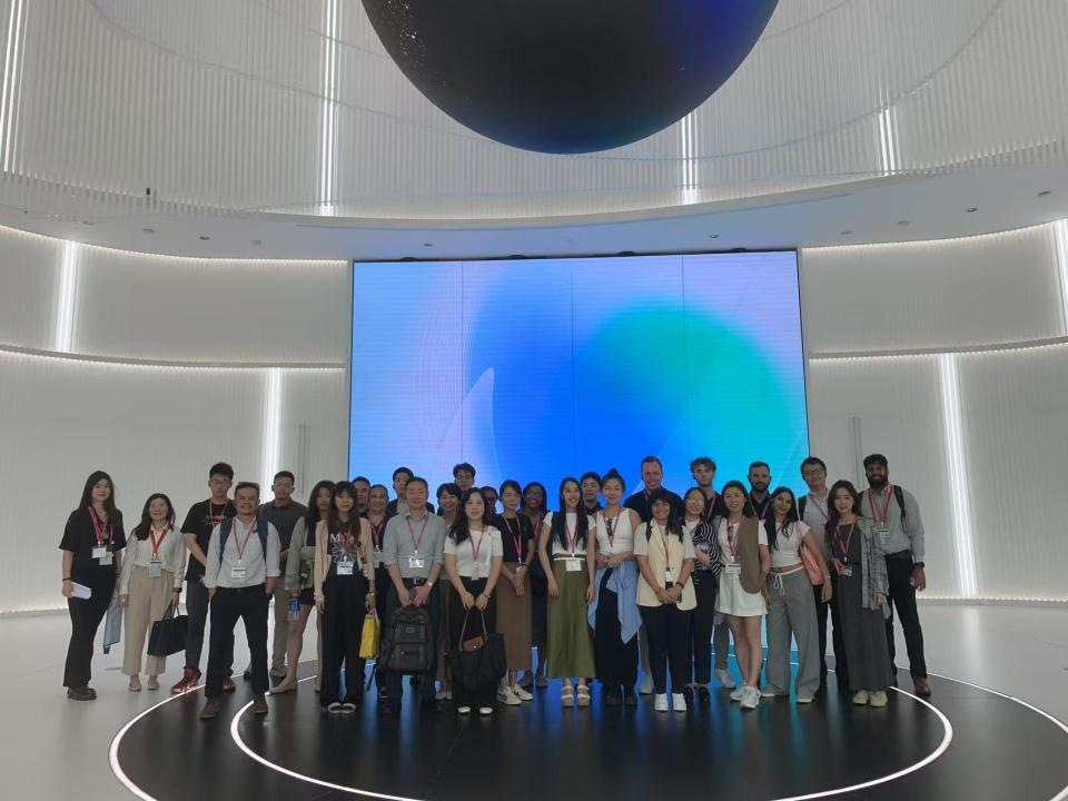 Group of UC Davis Graduate School of Management students and international peers standing together inside ByteDance headquarters in China. They are posed in front of a large digital display and surrounded by a modern, high-tech interior with glowing white walls.