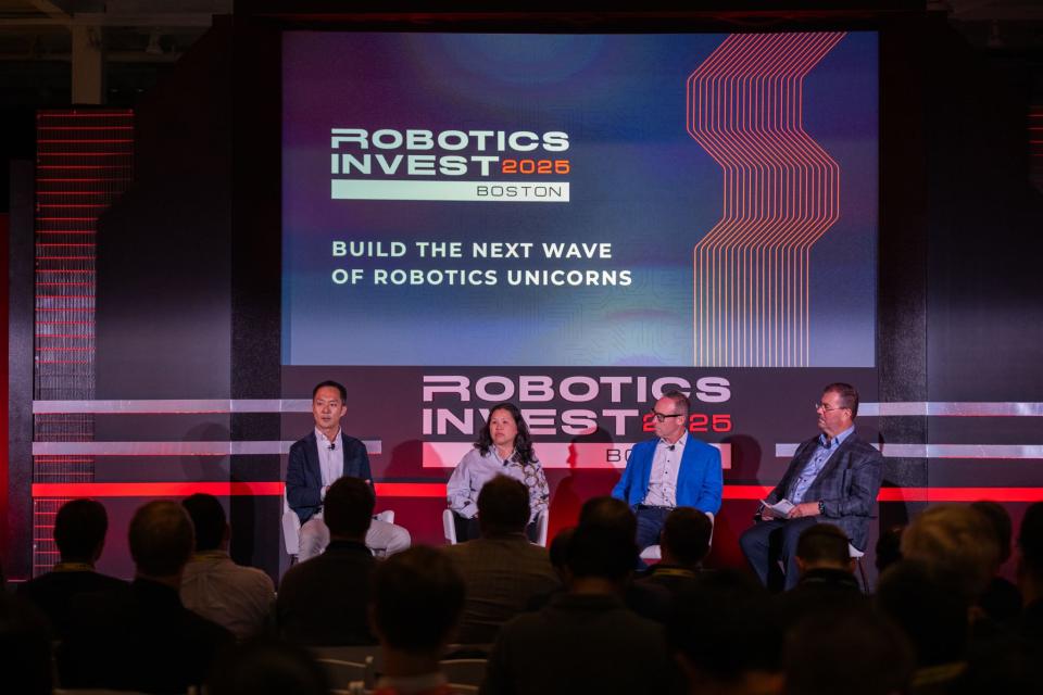 Koji Hasegaw with panelists speak onstage at Robotics Invest 2025 in Boston, seated in front of a large screen that reads “Build the Next Wave of Robotics Unicorns.” Audience members watch from the foreground.