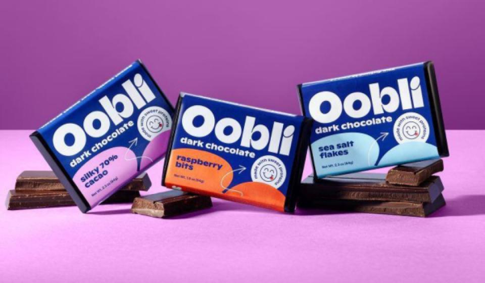 Oobli dark chocolate bars in Silky 70% Cacao, Raspberry Bits, and Sea Salt Flakes flavors displayed on chocolate squares against a purple background.