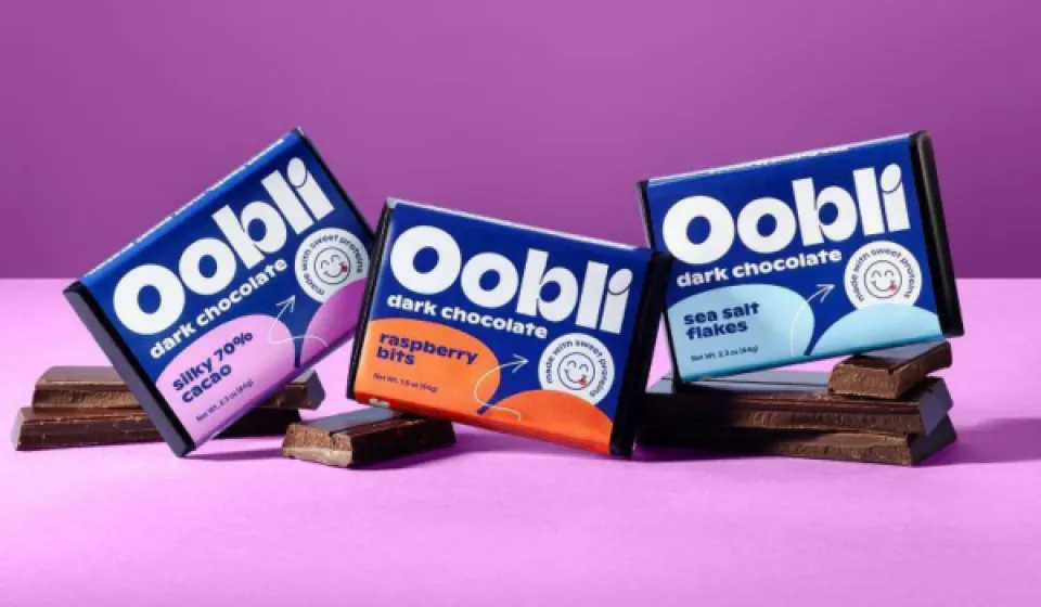 Oobli dark chocolate bars in Silky 70% Cacao, Raspberry Bits, and Sea Salt Flakes flavors displayed on chocolate squares against a purple background.