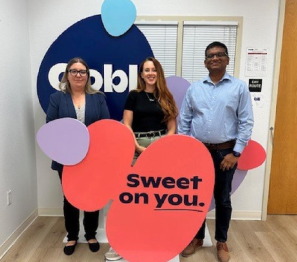 Three people stand in front of an Oobli display sign inside an office, holding colorful cutouts with the phrase “Sweet on you.”