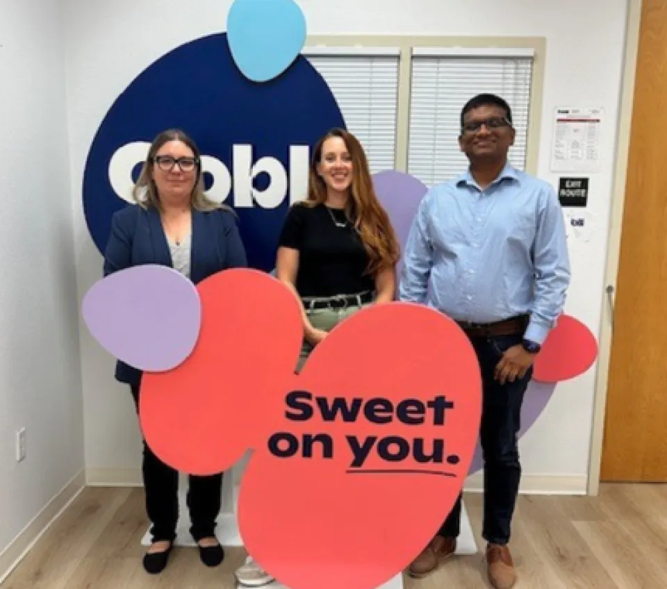 Three people stand in front of an Oobli display sign inside an office, holding colorful cutouts with the phrase “Sweet on you.”