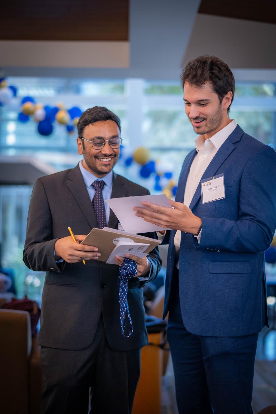 Daniel Vaziri and an MBA student reviewing documents during orientation, with blue and gold balloons decorating the background.
