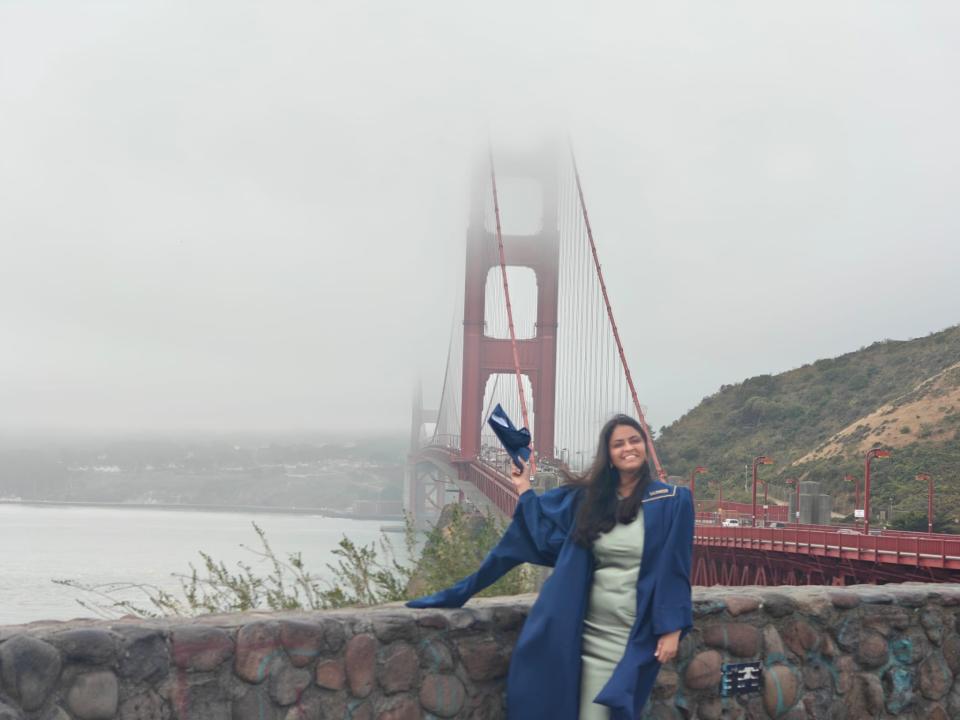 Shrishti Gupta wearing graduation robe in front of the Golden Gate bridge