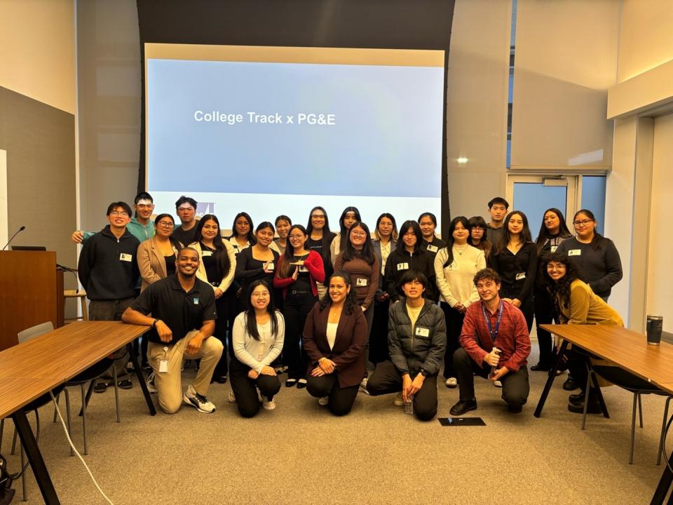 A large group of students and professionals posing for a group photo in a conference room. A presentation slide in the background reads “College Track x PG&E"