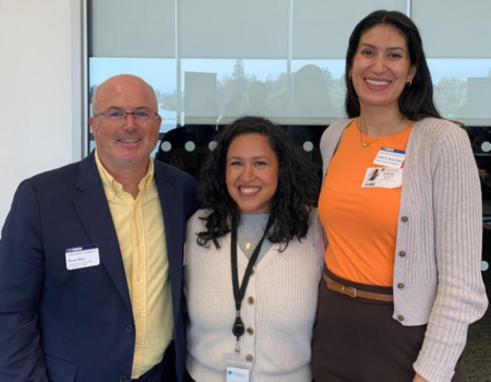Verenice Andrade and two UC Davis employees smiling and standing together indoors. They are wearing business attire with name badges, suggesting a professional networking or volunteer event.