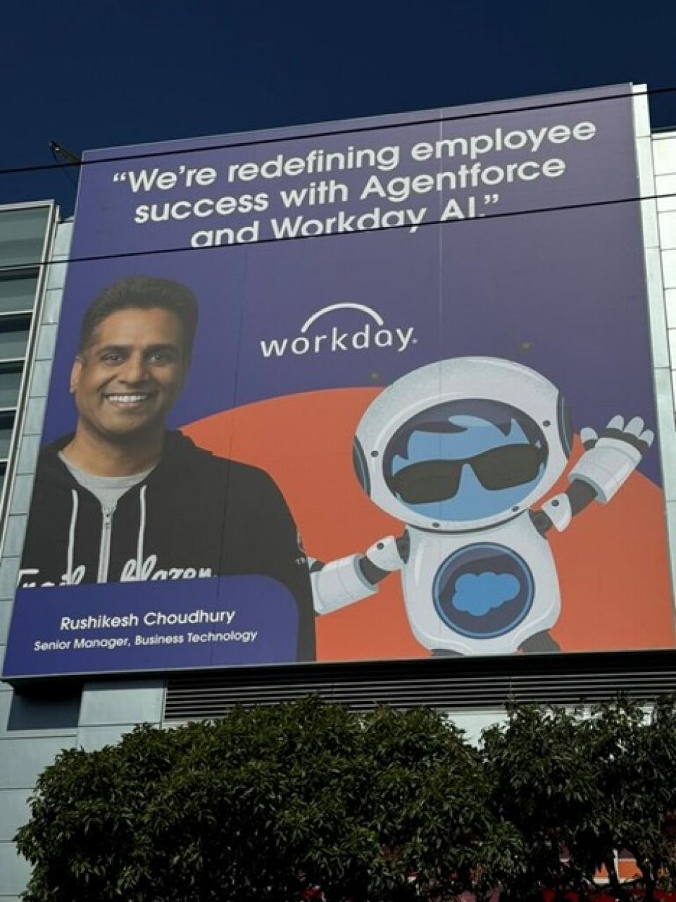 Large billboard featuring Rushikesh Choudhury, Senior Manager of Business Technology at Workday, alongside a cartoon robot. The text reads: “We’re redefining employee success with Agentforce and Workday AI.”