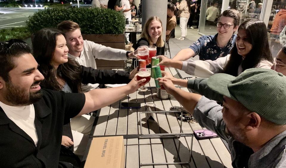 MBA students gathered around a table, toasting their drinks in the middle 