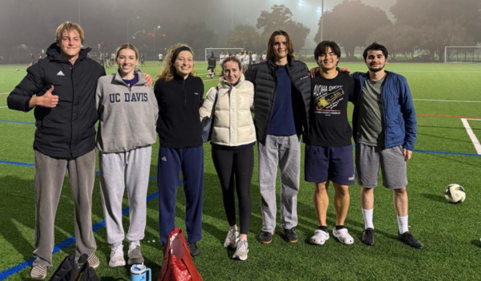 A group of UC Davis students stand together on a foggy soccer field at night, smiling after an intramural game.