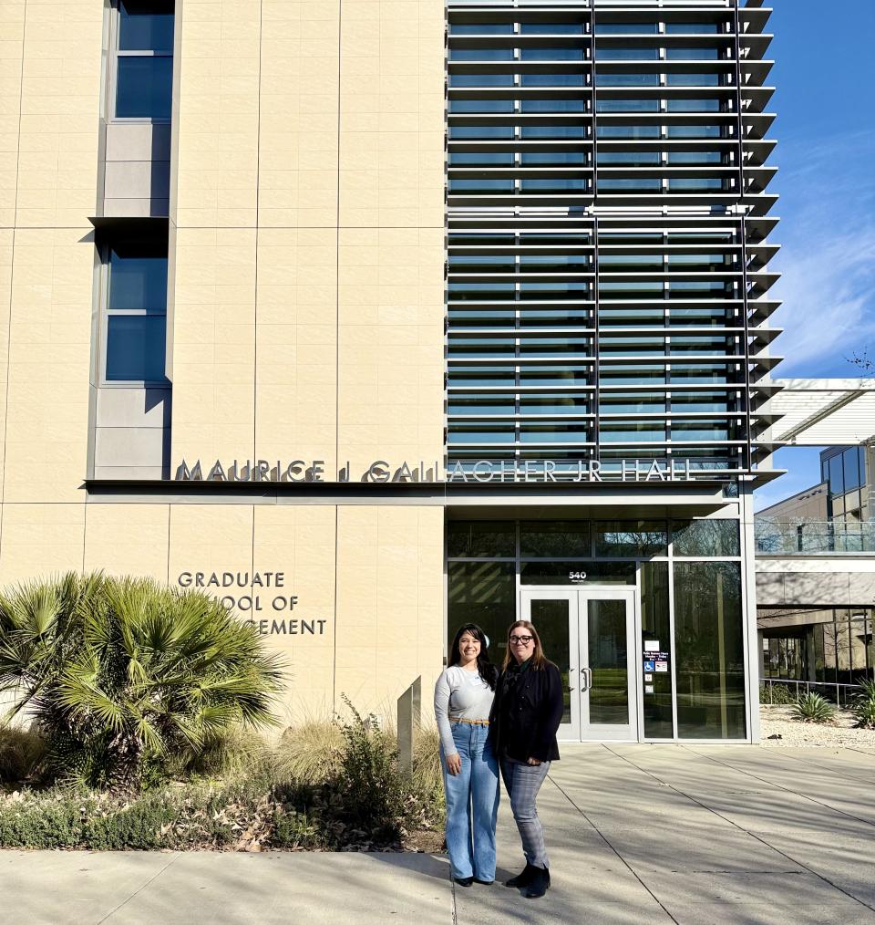 Two people stand in front of the entrance to Maurice J. Gallagher Jr. Hall, home to the Graduate School of Management, on a sunny day.
